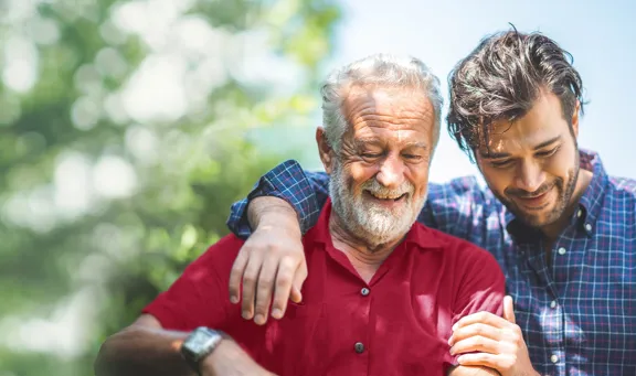 Two men smiling, the young man has his arm around the older man's shoulders