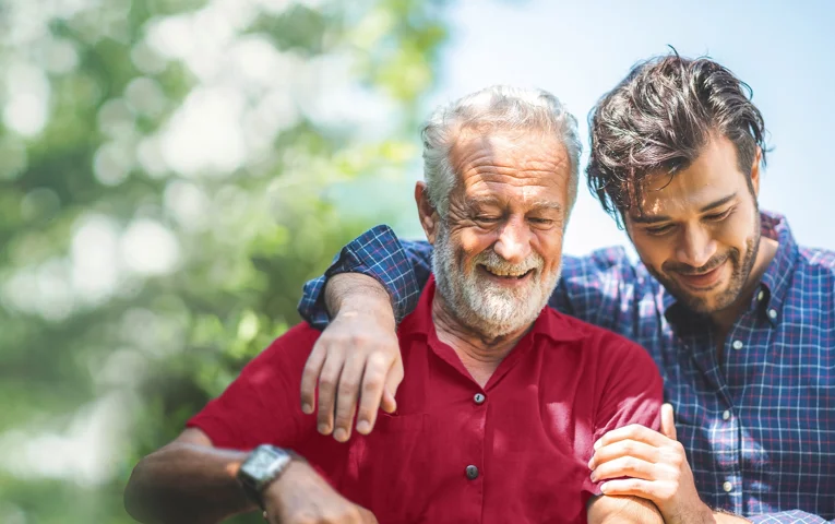 Two men smiling, the young man has his arm around the older man's shoulders