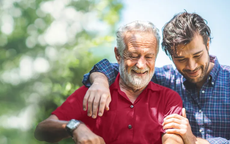 Two men smiling, the young man has his arm around the older man's shoulders